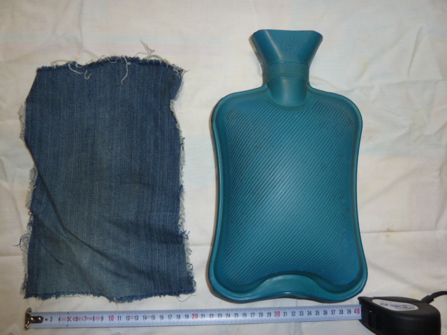 Photo of a blue rubber hot water bottle, view of the side with grid surface, with its Jeans' fabric piece. Dimensions of the hot water bottle are 7.8 width, 11.8 length, content 1.2 liter of water, 50.8 fl oz. Hot water bottle is used in Gardelle treatment method or to improve the work of the leaver.